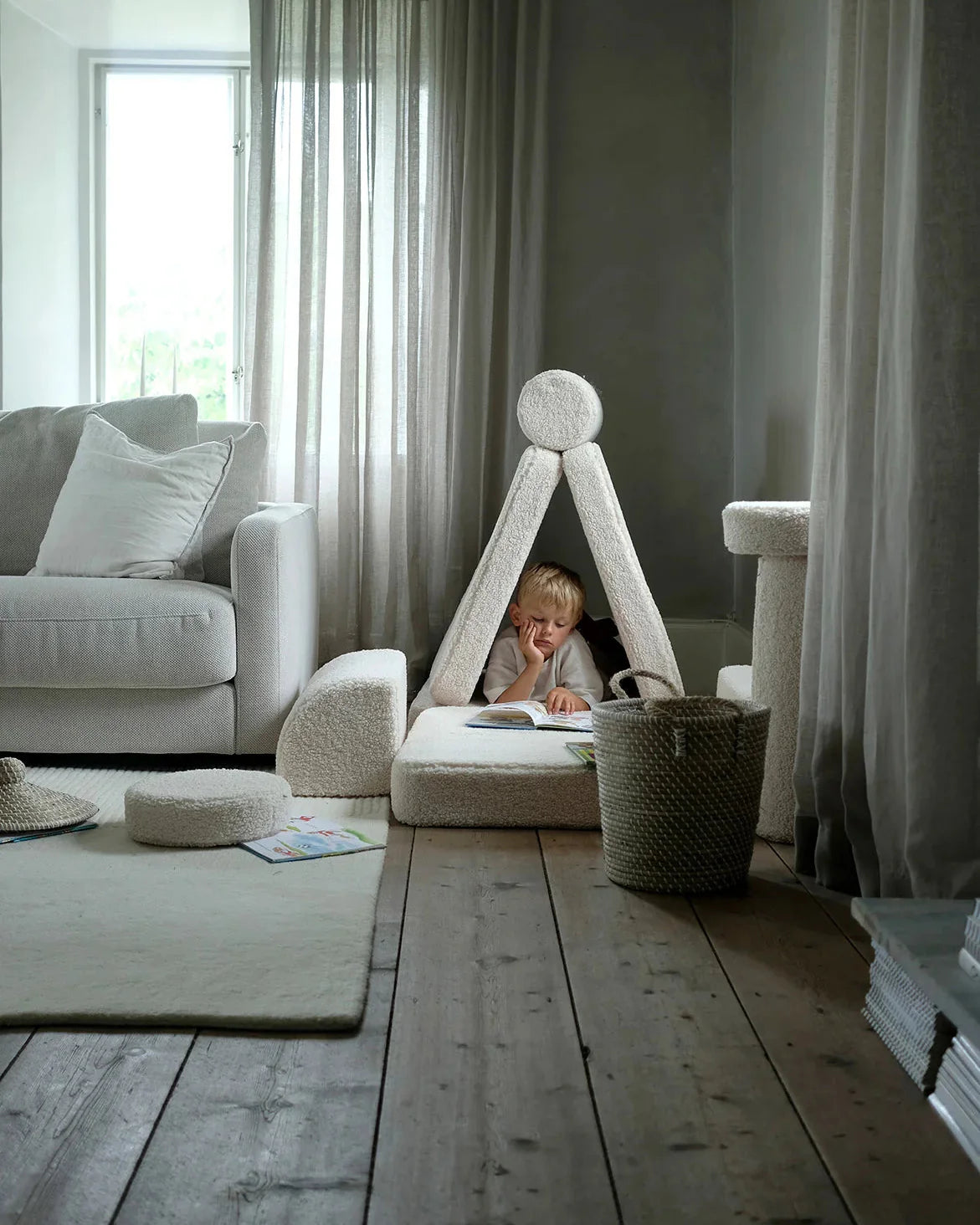 Child reading inside a small fort made with the Wigiwama Cream White Settee in a calm living room.