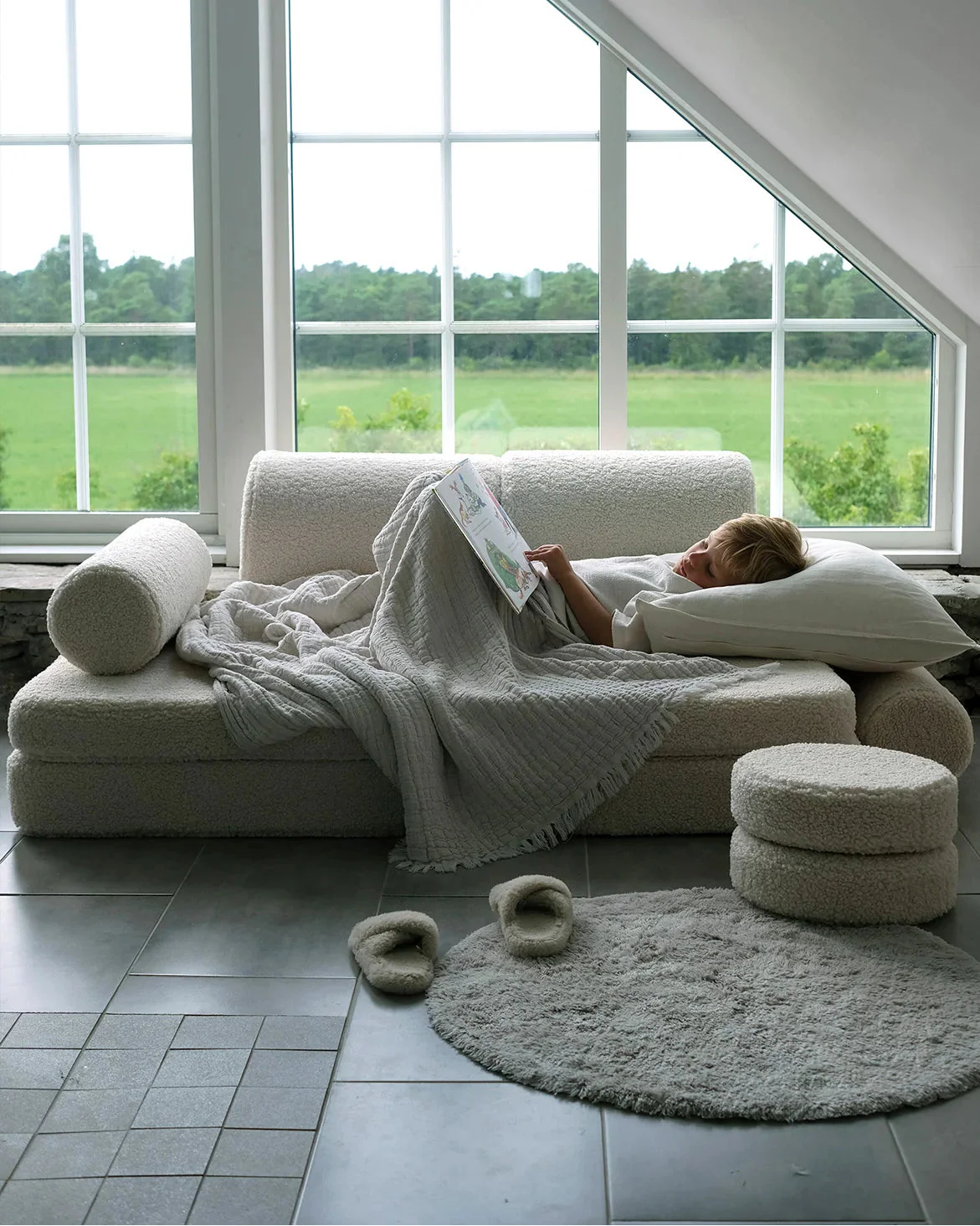 Child reading on the Wigiwama Cream White Settee in a cosy room with large windows and countryside view.