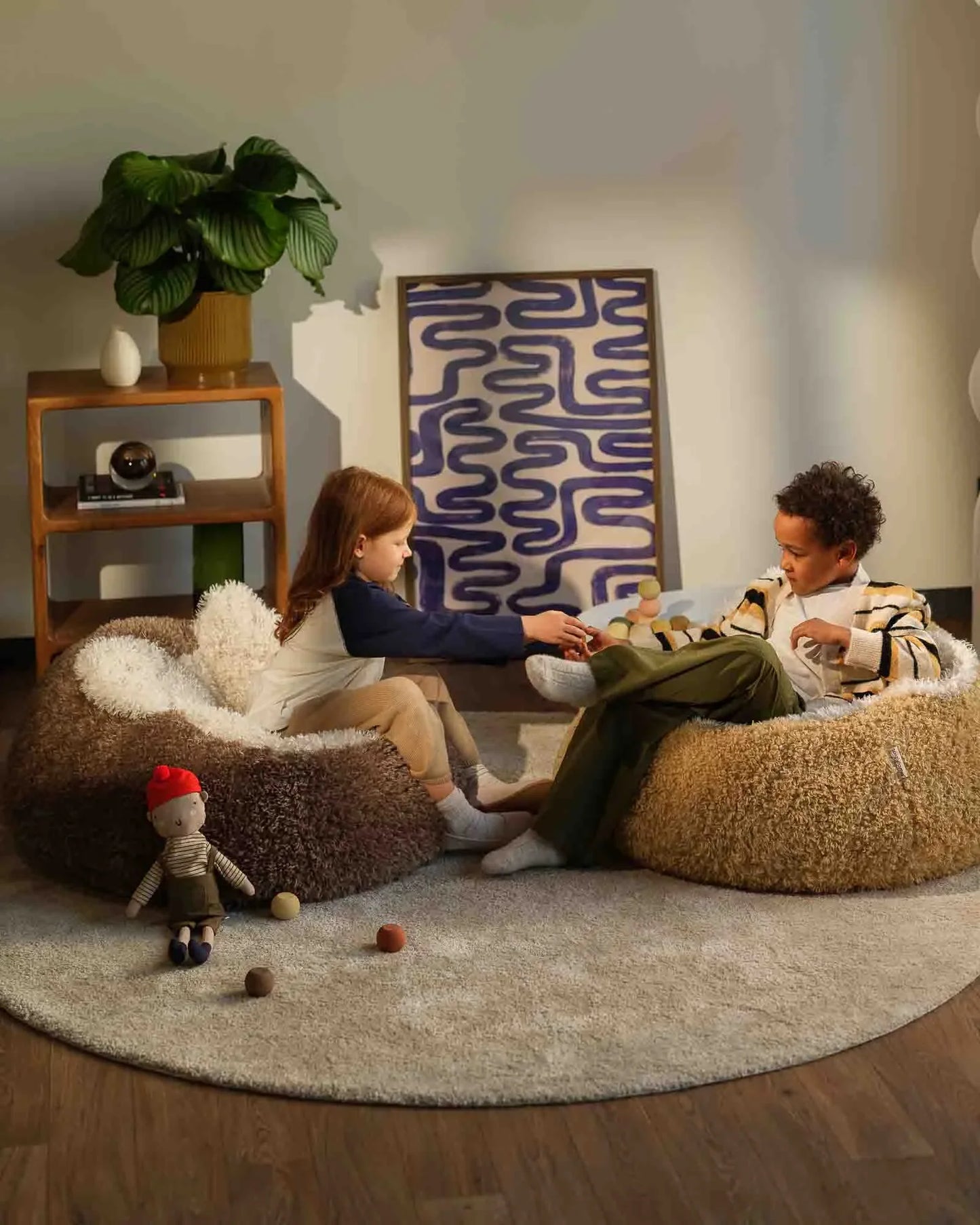 Two children playing with dolls on bean bags in a cozy living room.